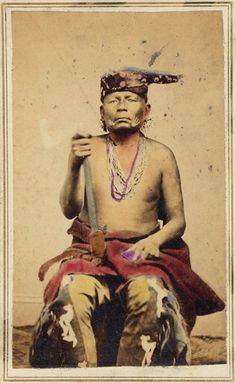 an old photo of a native american man with feathers on his head, holding a stick