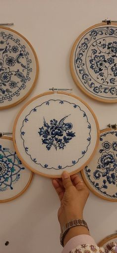 a person is holding up some embroiderys in front of four circular frames with blue flowers on them