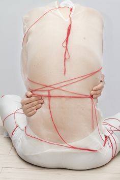 a woman is wrapped in plastic and tied up with red string on her back while sitting on the floor