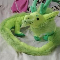 a green stuffed animal sitting on top of a bed next to two other stuffed animals