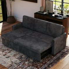 a grey couch sitting on top of a wooden floor next to a table and window