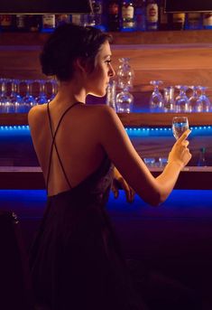 a woman sitting at a bar holding a wine glass in one hand and looking out the window