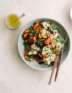 a bowl filled with vegetables and chopsticks next to a glass of orange juice