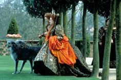 a woman in an orange dress is walking her dog on the grass near some trees