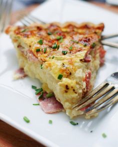 a slice of quiche with ham and cheese on a white plate next to a fork