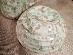 two green and brown vases sitting on top of a cloth covered tableclothed surface