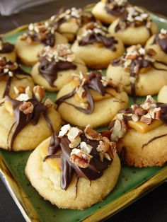 a green plate topped with lots of cookies covered in chocolate sauce and nuts on top