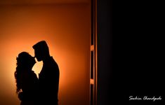 the silhouette of a man and woman kissing in front of an orange light