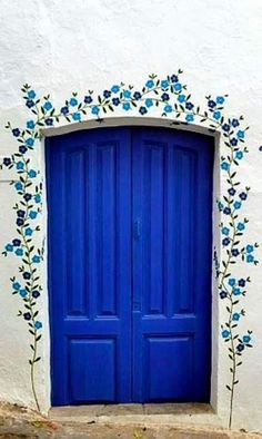 a blue door with flowers painted on the side of it in front of a white building