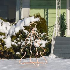 a small christmas tree made out of lights in front of a house with snow on the ground