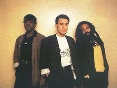 three men standing next to each other in front of a white wall and one man with dreadlocks