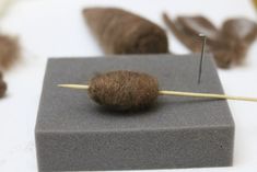 a wool ball on a stick with needles sticking out of the end, surrounded by feathers