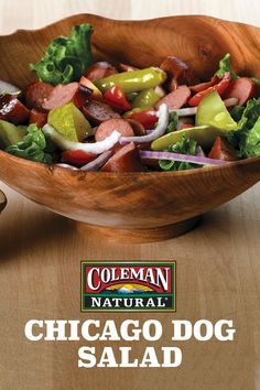 a wooden bowl filled with lettuce, peppers and sausage on top of a table