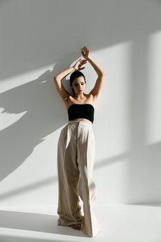 a woman standing in front of a white wall with her hands behind her head and arms above her head