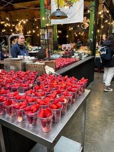 people are shopping at an outdoor market with tomatoes on the table and buckets full of them