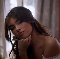 a woman sitting on top of a bed with her hand under her chin and looking off to the side