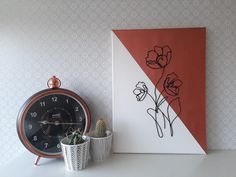 an alarm clock sitting next to a painting on a wall with flowers drawn on it