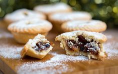 several small pastries on a wooden cutting board with powdered sugar around the edges