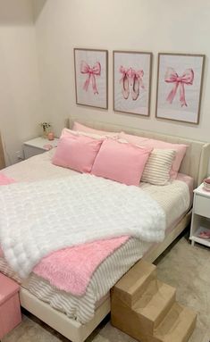 a white bed with pink pillows and two pictures on the wall next to it's foot steps