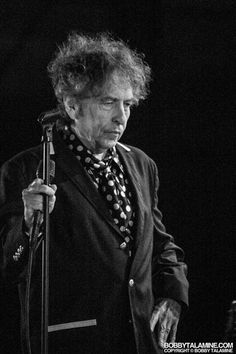 a man with curly hair holding a microphone in front of him and wearing a suit