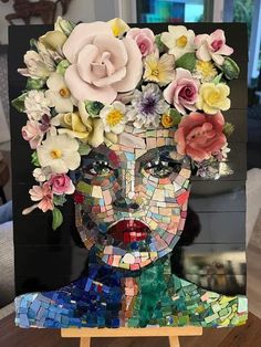 a mosaic art piece with flowers on it's head, sitting on a easel