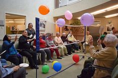 a group of people sitting in chairs with balloons and streamers flying around the room