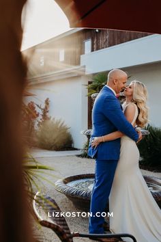 a bride and groom kissing in front of a fountain at their outdoor wedding ceremony with the sun shining on them