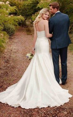 a bride and groom standing in the middle of a dirt path with trees behind them