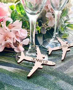 two personalized wooden wine glasses and an airplane ornament on a table with pink flowers