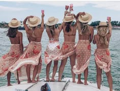 six women in matching bathing suits standing on a boat and raising their hands to the sky