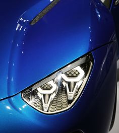 the front end of a blue sports car with its lights on and chrome grills