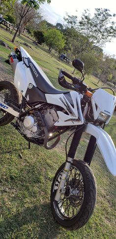 a white and black motorcycle parked on top of a grass covered field next to trees