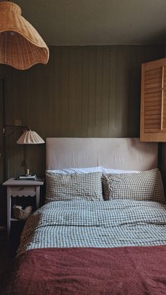 a bed sitting under a lamp next to a wooden headboard and night stand in a bedroom