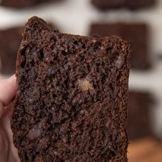 a hand holding a piece of brownie in front of a brick wall with white bricks