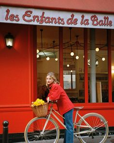 a woman riding a bike down a street next to a red building with french writing on it