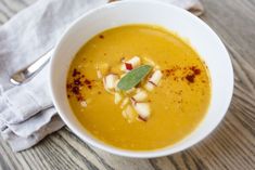 a white bowl filled with soup on top of a wooden table next to a napkin