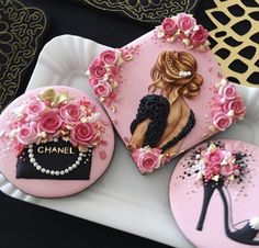 three decorated cookies on a plate with pink icing and black accents, one has a lady's purse