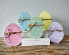 four painted eggs tied with twine and sitting on a wooden block in front of a white wall