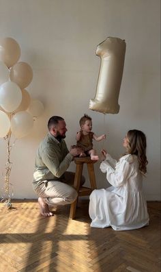 a man, woman and child sitting on a chair with balloons in the air