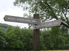 two wooden signs pointing in opposite directions to west highland way and west highland way with trees in the background