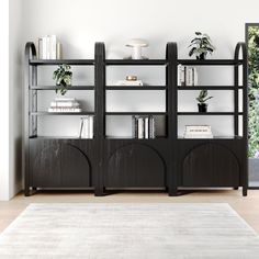 a black bookcase with books and plants on it in front of a white wall