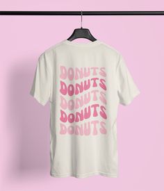 Let's indulge in everyone's favorite sweet treat with our Unisex Donuts T-Shirt! This comfort colors tee is an irresistible choice for pastry enthusiasts, breakfast lovers, coffee shop regulars, and anyone who can't say no to a delectable donut. This unique comfort colors tee is a delightful and tantalizing way to flaunt your love for these sugary delights. Whether you're enjoying a morning coffee, visiting a local bakery, or just relaxing at home, this Donuts T-shirt is a fabulous addition to y Fun Short Sleeve T-shirt With Logo Print, White Print Text T-shirt With Fun Style, Fun White Print Text T-shirt, Fun White T-shirt With Text Print, Bakery T Shirt Design, Retro Pink Printed T-shirt, Donut Shirt Ideas, Donut Tshirt Design, Donut Care