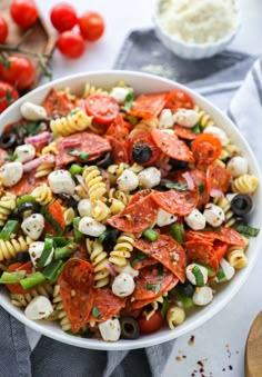 A white bowl filled with pizza pasta salad surreounded by cherry tomatoes, grated parmesan and a wooden spoon. Pasta Pepperoni, Easy Pizza Pasta, Pizza Pasta Salad, Meatless Pasta, Potluck Salad, Salad Appetizer Cups, Salads Ideas, Appetizer Cups, Mozzarella Balls