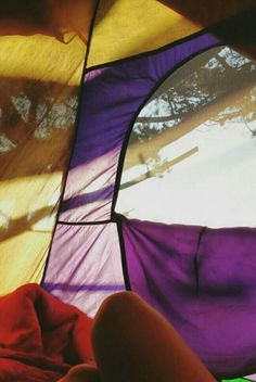 a person laying in front of a purple and yellow tent