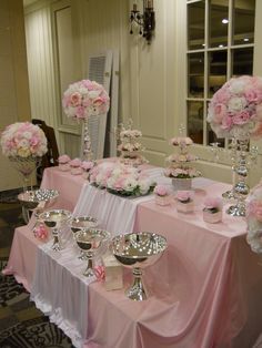 a table topped with lots of pink flowers and silver dishes covered in white frosting