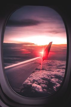 an airplane wing with the sun setting in the sky and clouds as seen from inside