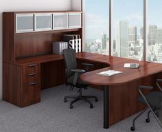 an office cubicle with desk, chair and bookcase in front of large windows