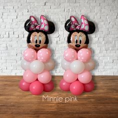 two minnie mouse balloons sitting on top of a wooden table next to a brick wall