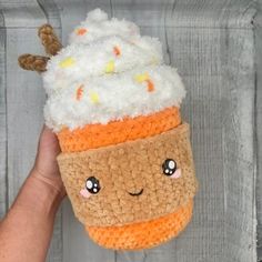 a hand holding up a small crocheted cup with a smiling face on it