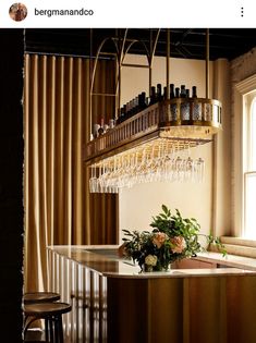 a bar with wine glasses hanging from it's ceiling and flowers on the counter